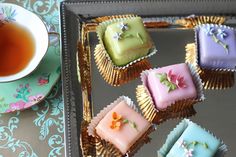 there are many small cakes on the tray next to a cup of tea and saucer