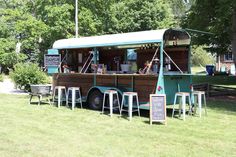 an old fashioned food truck is parked in the grass with stools and tables around it