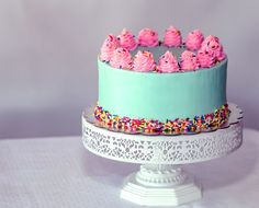 a blue cake with pink frosting and sprinkles on a white pedestal