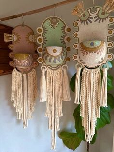 three decorative masks hanging on a wall next to a potted plant with green leaves