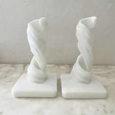 two white vases sitting on top of a marble countertop next to each other