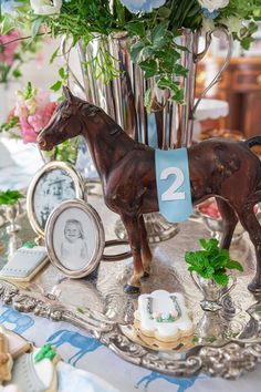 a horse figurine sitting on top of a silver tray with flowers in the background