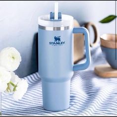 a blue travel mug sitting on top of a table next to white flowers and plates