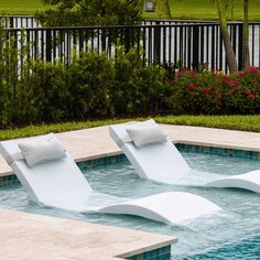 two white lounge chairs sitting on top of a swimming pool