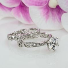 two wedding rings sitting next to each other on top of a table with flowers in the background