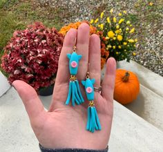 a person's hand with two blue earrings on it and some pumpkins in the background