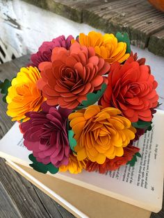 colorful paper flowers are on top of an open book in front of a wooden bench