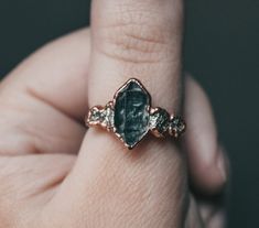 a close up of a person's hand holding a ring with a green stone