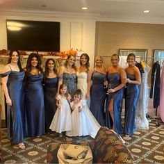 a group of women standing next to each other in front of a dress rack with dresses on it