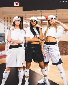 three women in matching outfits posing for a photo together on a swing set at an indoor basketball court