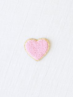 a pink and gold heart shaped brooch sitting on top of a white fabric covered surface