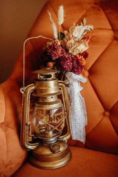 an old fashioned lantern with flowers in it on top of a brown chair next to a pillow