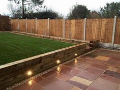 an outdoor garden with lights on the ground and grass in the back yard, next to a wooden fence