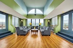 a living room filled with furniture next to large windows on top of a hard wood floor