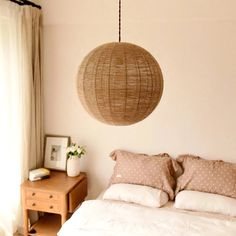 a bed with white sheets and pillows under a hanging light fixture above the headboard