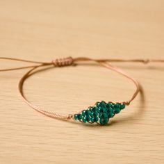 a string bracelet with a green beaded christmas tree on it sitting on a wooden surface