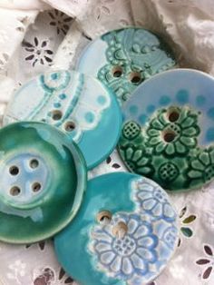 four buttons are sitting on top of a lace doily, one is green and the other is blue