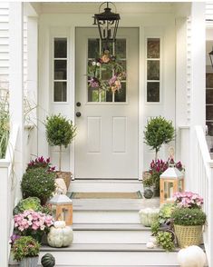 the front porch is decorated for fall with flowers, pumpkins and lanterns on the steps