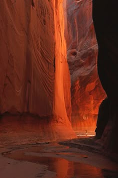 a narrow slot in the side of a mountain with water running through it and light shining on the ground