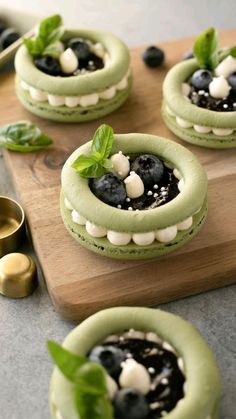 four green desserts with blueberries and mint leaves in them on a cutting board