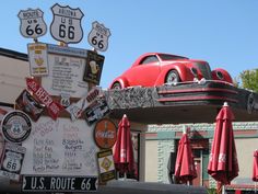 an old red car is parked in front of a route 66 sign and umbrellas