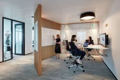 three people are in an office setting with whiteboards on the wall