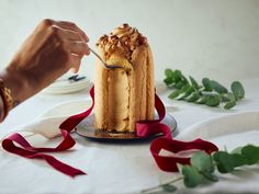 a person is cutting into a cake on a table with red ribbon and greenery