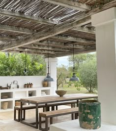 an outdoor kitchen and dining area with wood beams on the ceiling, tile flooring and white walls