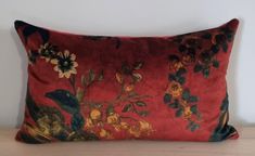 a red pillow with flowers on it sitting on top of a wooden table next to a white wall