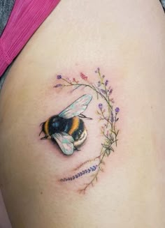 a woman's stomach with a bee and flowers tattoo on the side of her belly