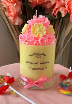 a yellow candle with pink and yellow flowers in it sitting on a table next to lollipops