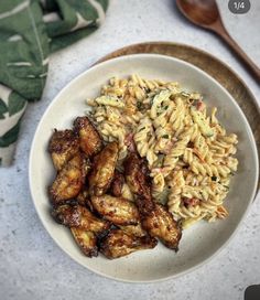 a white bowl filled with pasta and chicken wings on top of a table next to a wooden spoon