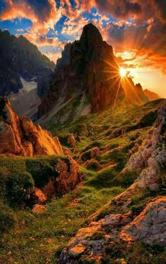 the sun shines brightly through the clouds over some rocks and grass on a mountain