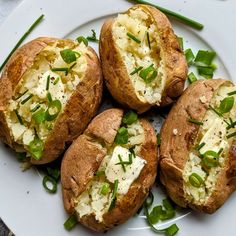 four baked potatoes with cheese and green onions on a white plate, ready to be eaten