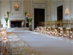 the aisle is lined with white flowers and candles for an elegant wedding ceremony in front of a fireplace