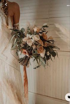 a woman in a wedding dress holding a bridal bouquet with dried flowers and greenery