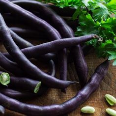 some purple carrots and green leaves on a wooden table with seeds next to them