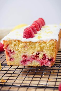 a close up of a cake on a cooling rack with raspberries and lemons