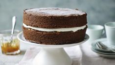 a chocolate cake sitting on top of a white plate next to cups and saucers