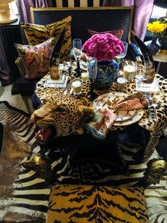 the table is set with plates, flowers and vases on zebra - print fabric