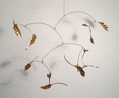 a metal wind chime with leaves hanging from it's sides on a white wall