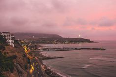 an ocean view at dusk with the lights on and cars parked along the shore line