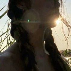 a woman with braids standing in front of palm trees and the sun behind her