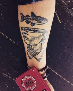 a person with a tattoo on their leg holding a red suitcase and a fish sticker