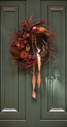 a green door with a wreath hanging on it's side and an autumn decoration