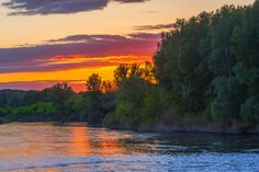 the sun is setting over a river with trees on both sides and clouds in the sky