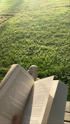 an open book sitting on top of a wooden bench next to a lush green field