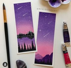 two cards with mountains and trees on them next to paintbrushes, watercolors and other items