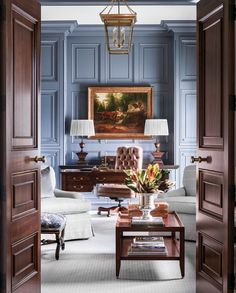 a living room with blue walls and wooden doors leading to a sitting area that has a painting on the wall