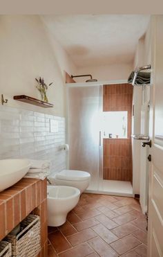 a white toilet sitting next to a sink in a bathroom under a window on top of a tiled floor